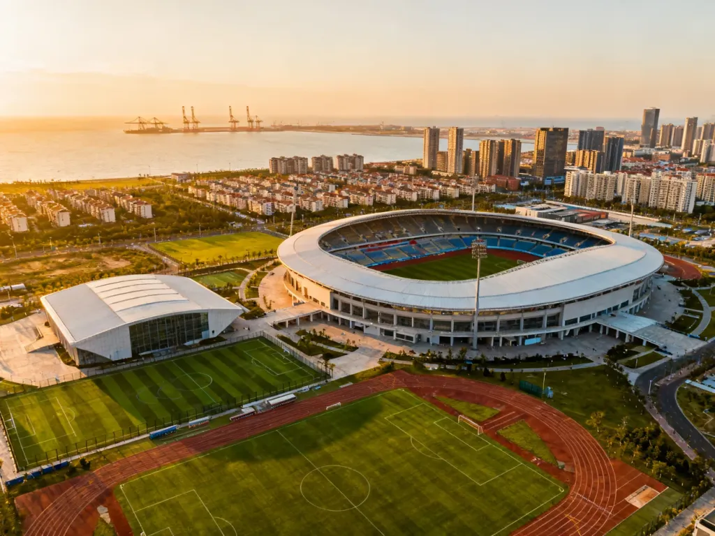 Panorama gdańskiego kompleksu sportowego ze stadionem i halą, otoczonego boiskami oraz zabudową miasta w tle, no text on the picture