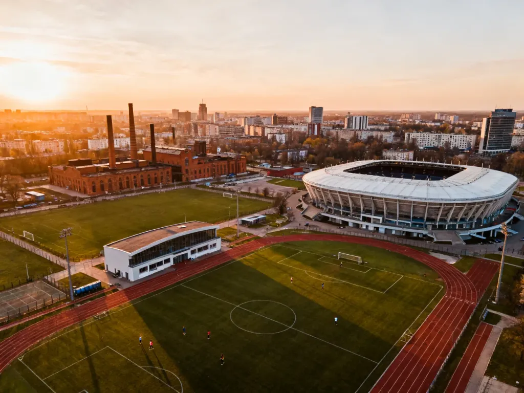 Panorama sportowej dzielnicy Łodzi z dużym stadionem, halą i bieżnią w ciepłym świetle zachodu, no text on the picture