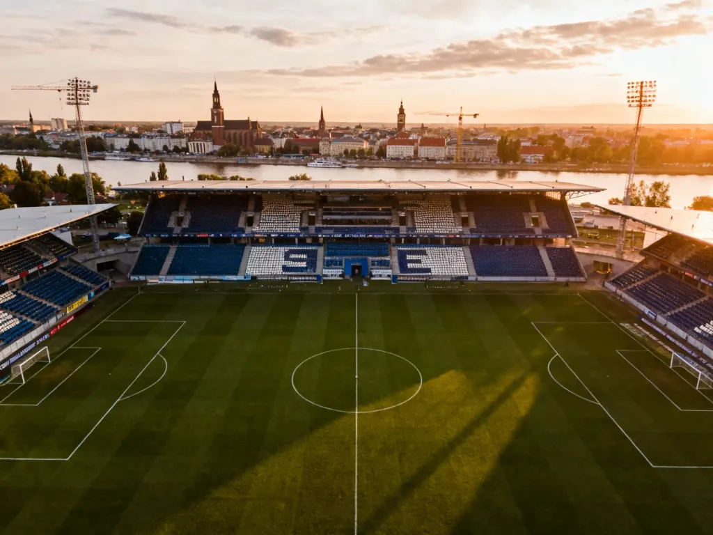 Nowoczesny stadion piłkarski w Szczecinie o zachodzie słońca, z panoramą miasta i Odry w tle, no text on the picture